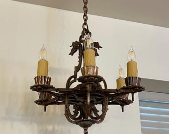 May include: Ornate bronze chandelier with five candle-style lights. The fixture has a decorative chain and intricate metalwork, including floral and scroll designs. The bulbs are encased in faux candle sleeves.