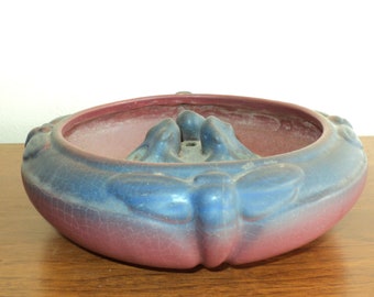 May include: A blue and pink ceramic planter with a decorative design of stylized butterflies and a central raised area with a hole. The planter has a crackled glaze finish.