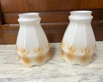 May include: Two white glass lampshades with a scalloped edge and a floral design in shades of brown.