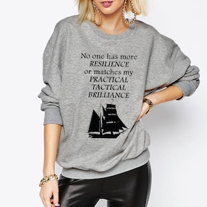 Peut inclure: Sweat-shirt gris avec un graphique de voilier noir et le texte "No one has more RESILIENCE or matches my PRACTICAL TACTICAL BRILLIANCE."