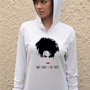 Op de afbeelding: Een wit longsleeve hoodie met een zwart-witte illustratie van een gezicht en de tekst "WHY CAN'T I BE YOU?" gedrukt op de voorkant.