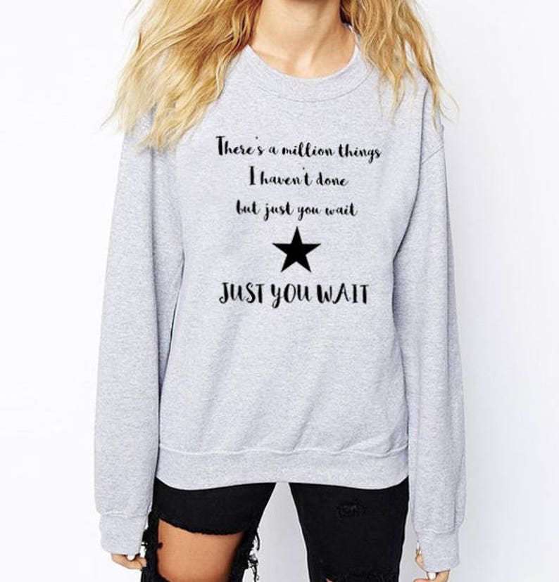 K&ouml;nnte beinhalten: Grauer Pullover mit einem schwarzen Stern und dem Text "There's a million things I haven't done but just you wait JUST YOU WAIT"