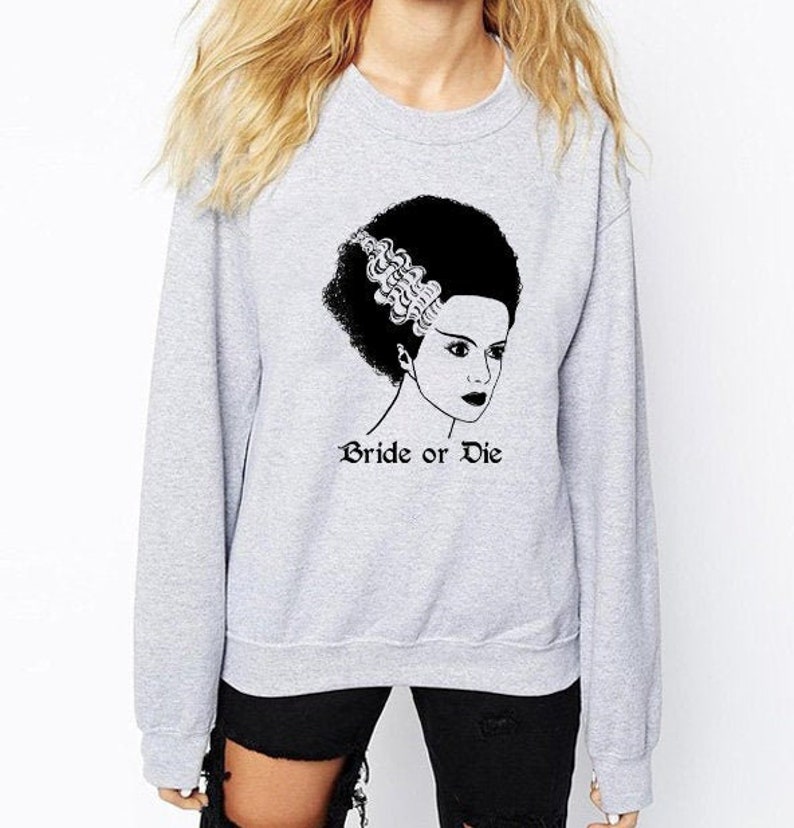 K&ouml;nnte beinhalten: Grauer Pullover mit einer schwarz-wei&szlig;en Illustration einer Frau mit einer Frisur, die an die Braut von Frankenstein erinnert. Der Text "Bride or Die" ist unter der Illustration aufgedruckt.