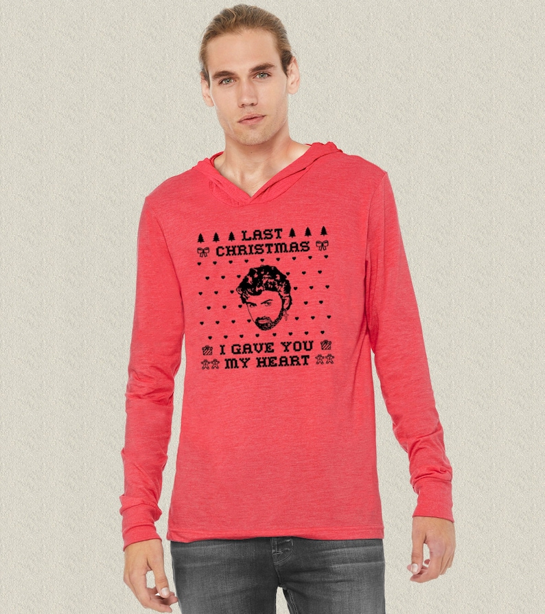 Op de afbeelding: Een rood langarm hoodie met een zwart-witte grafische print van een mannengezicht en de tekst "Last Christmas I Gave You My Heart".