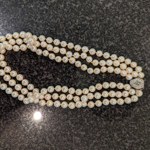 May include: A triple-strand pearl necklace with a decorative clasp. The pearls are a creamy white hue and appear uniform in size. The clasp is silver-toned and features small, clear stones.