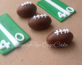 May include: Brown football-shaped decorations with white laces and green rectangular field markers with white yard line and the number 40. The image has the text "FancyTop CupCake".