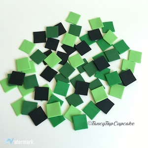 May include: A collection of green and black fondant squares, perfect for decorating cakes or cupcakes.  The squares are arranged in a random pattern on a white background.
