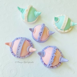 May include: Five pastel-colored fondant cupcake toppers shaped like hats with horns. The toppers are decorated with white lace and purple or blue accents. The toppers are on a white background. @FancyTopCupcake