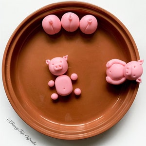 May include: A brown ceramic plate with pink fondant pig figurines. There are three small pig figurines and two larger pig figurines. One of the larger pig figurines is standing and the other is lying down.