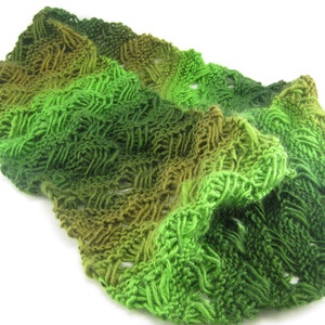 May include: A green and brown knitted scarf with a textured pattern. The scarf is made of soft yarn and has a gradient of color from dark green to light green.