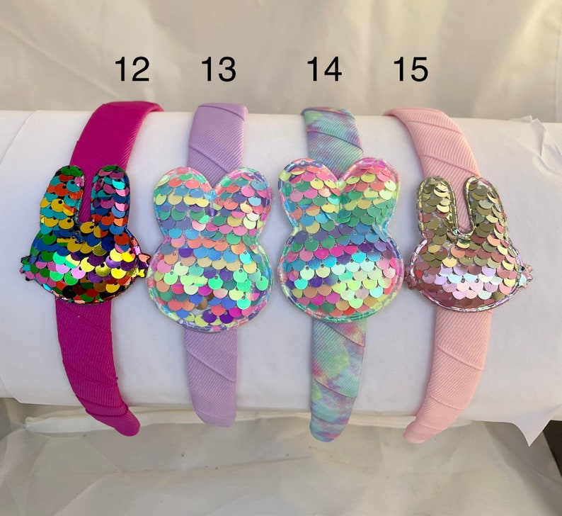 May include: Four headbands with different colors and designs. Each headband has a sequin bunny attached. The headbands are labeled 12, 13, 14, and 15.