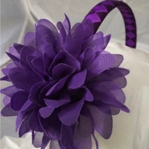 May include: Purple headband with a large purple flower attached. The headband is made of a patterned fabric.
