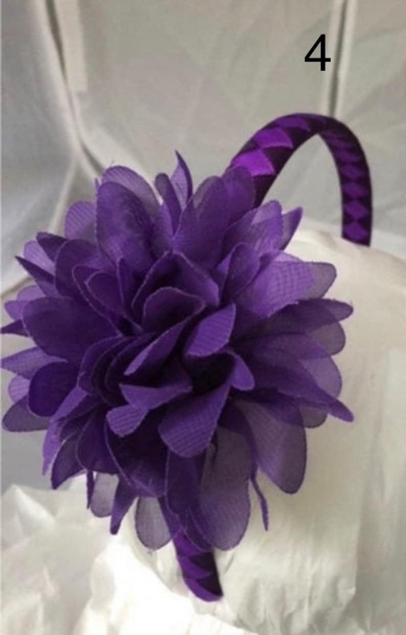 May include: Purple headband with a large purple flower attached. The headband is made of a patterned fabric.