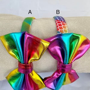 May include: Two rainbow iridescent metallic hair bows with a headband. One headband has a rainbow stripe pattern and the other has a mermaid scale pattern.