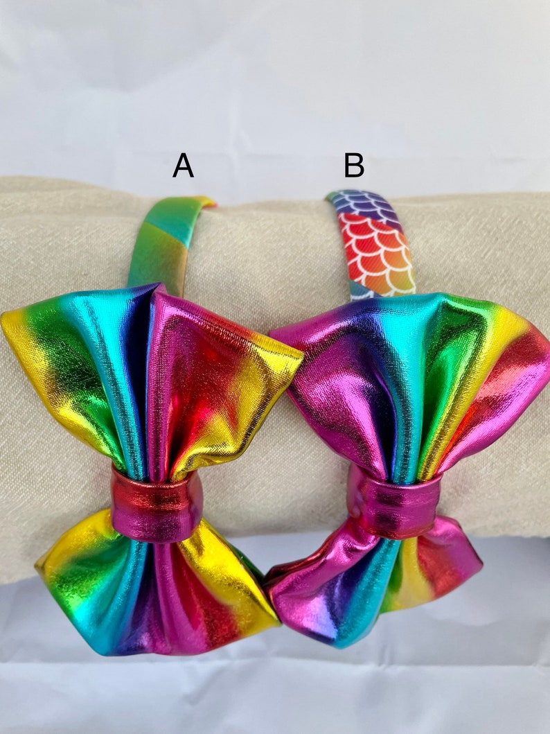 May include: Two rainbow iridescent metallic hair bows with a headband. One headband has a rainbow stripe pattern and the other has a mermaid scale pattern.
