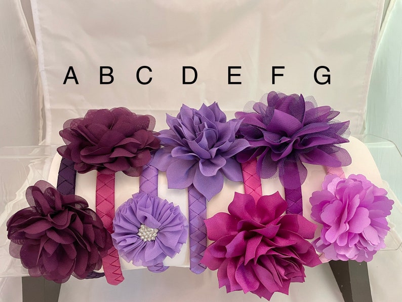 May include: Seven purple and lavender fabric flower headbands with different styles and textures. The headbands are labeled A through G.