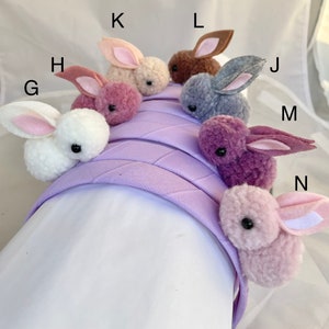 May include: A purple headband with nine fuzzy bunny charms in various colors, including pink, white, gray, brown, and purple. The headband is made of a soft, plush material and is perfect for adding a touch of whimsy to any outfit.