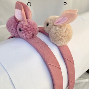 May include: Two pink headbands with fuzzy bunny ears. One bunny is pink and the other is cream colored.
