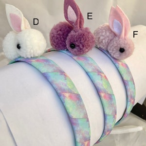 May include: Three headband hair accessories with fuzzy bunny charms. The headbands are tie-dye patterned in shades of blue, pink, and purple. The bunny charms are white, purple, and light pink.