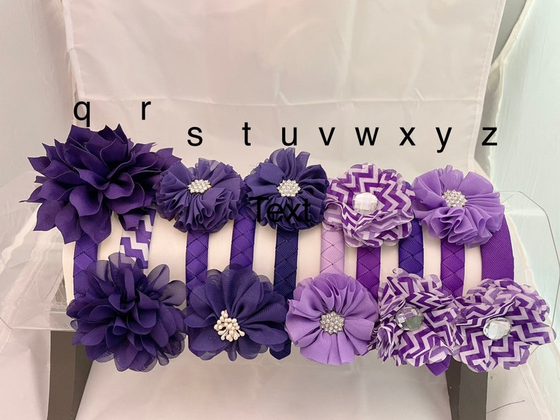 May include: Set of 9 purple and lavender fabric headbands with various flower and chevron designs. The headbands are labeled with the letters q, r, s, t, u, v, w, x, y, and z.