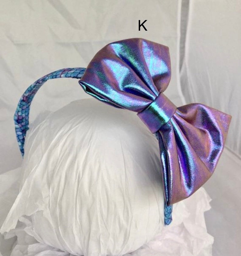 May include: A headband with a large iridescent purple bow. The headband is decorated with a blue and white pattern.