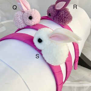 May include: Three pink headbands with fuzzy bunny rabbit charms. The bunnies are pink, purple, and white. The headbands are all pink.