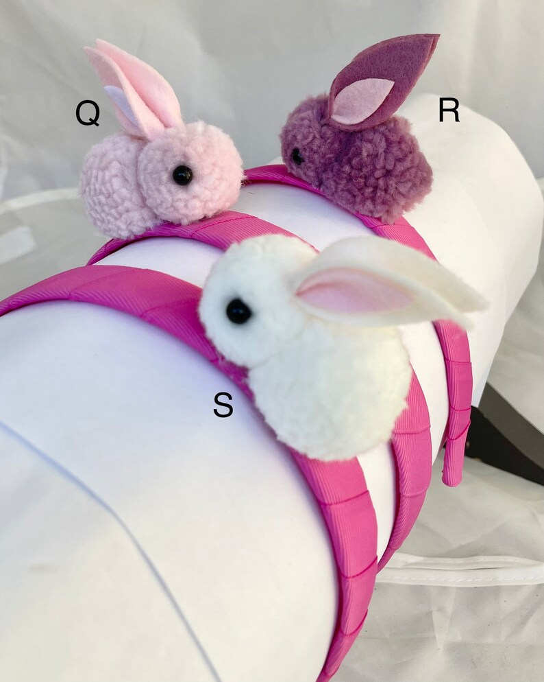 May include: Three pink headbands with fuzzy bunny rabbit charms. The bunnies are pink, purple, and white. The headbands are all pink.