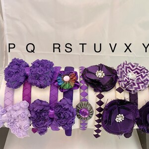 May include: A set of nine purple and white headbands with various fabric embellishments, including bows, flowers, and geometric patterns. The headbands are labeled P, Q, R, S, T, U, V, X, and Y.