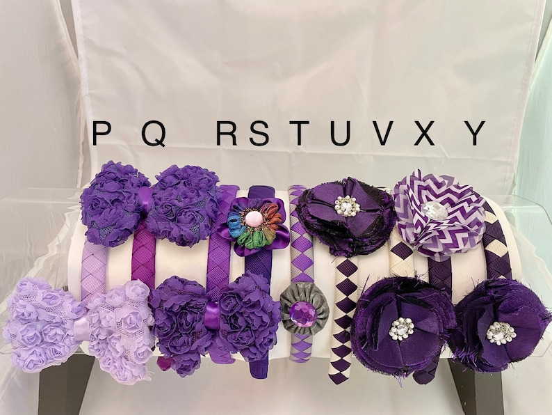 May include: A set of nine purple and white headbands with various fabric embellishments, including bows, flowers, and geometric patterns. The headbands are labeled P, Q, R, S, T, U, V, X, and Y.