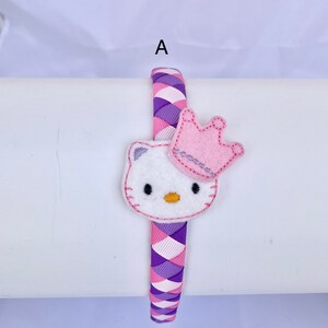 May include: A purple and pink braided headband with a white felt Hello Kitty character wearing a pink crown.