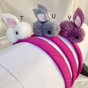 May include: Three fuzzy bunny headbands in white, gray, and purple. The headbands are pink and made of fabric.