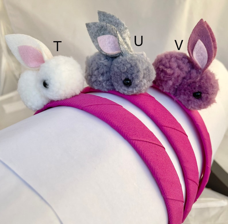 May include: Three fuzzy bunny headbands in white, gray, and purple. The headbands are pink and made of fabric.