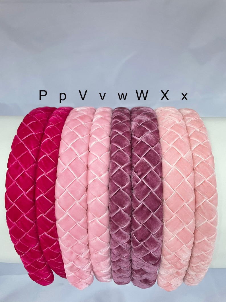 May include: Six velvet headbands in different shades of pink and red. The headbands are arranged in a row from left to right, with the darkest shade on the left and the lightest shade on the right. The headbands are all quilted with a diamond pattern.