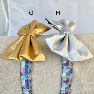 May include: Two hair headbands with a gold and silver bow. The headbands have a mermaid scale pattern.