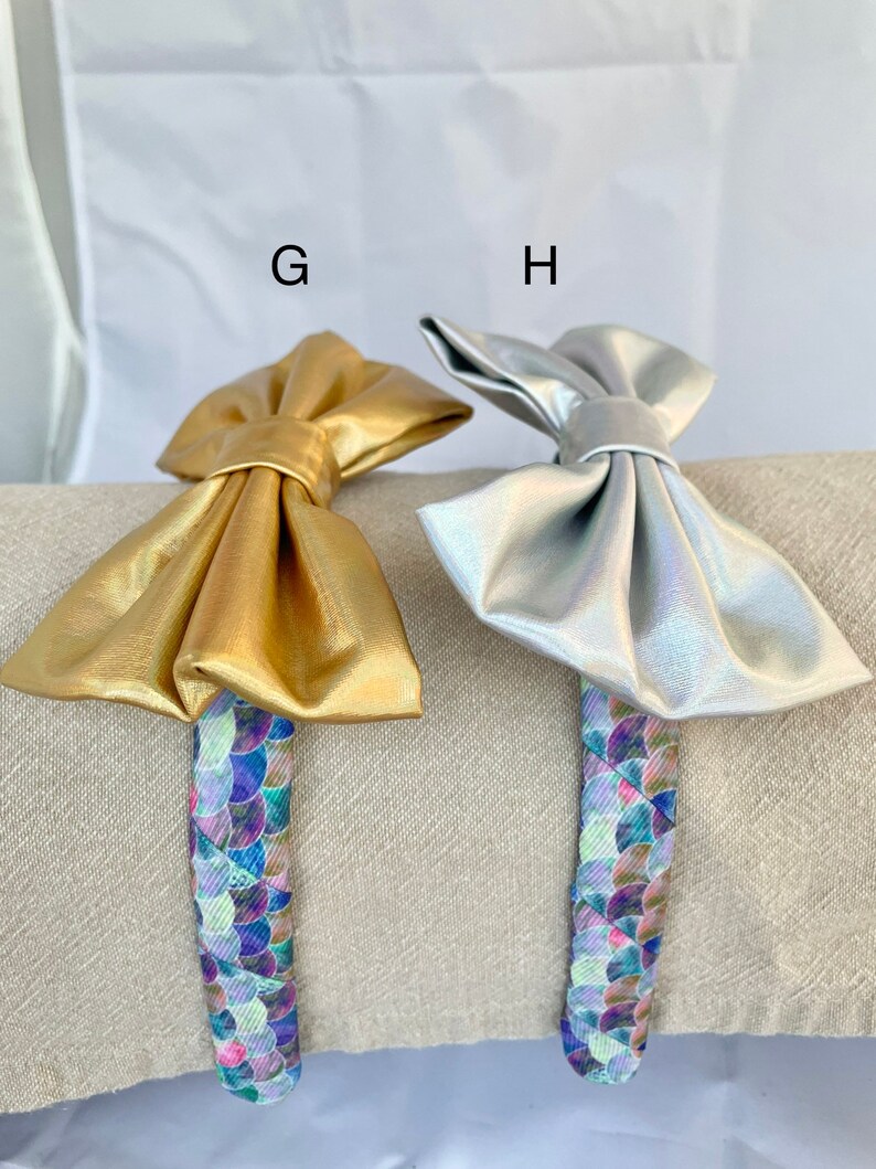 May include: Two hair headbands with a gold and silver bow. The headbands have a mermaid scale pattern.