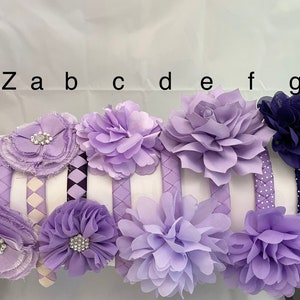 May include: Set of eight purple and navy blue headbands with various flower embellishments. The headbands have different patterns, including polka dots, plaid, and woven.
