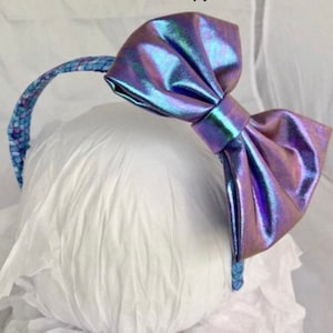 May include: A headband with a large iridescent purple bow. The headband is made of a blue and purple patterned fabric.