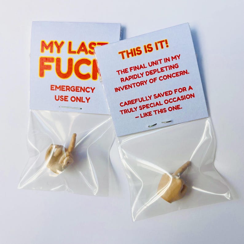 Op de afbeelding: Twee kleine plastic zakjes met elk een miniatuurhand die de middelvinger opsteekt. Elk zakje heeft een witte kaart met rode en oranje tekst. E&eacute;n kaart leest "MY LAST FUCK EMERGENCY USE ONLY." De andere leest "THIS IS IT!" en andere tekst.