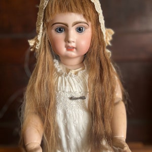 May include: Antique porcelain doll with long blonde hair, wearing a white lace dress and a white lace bonnet.