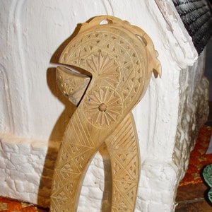 May include: A wooden nutcracker with intricate carvings in a geometric pattern. The nutcracker is light brown and has a rounded shape.