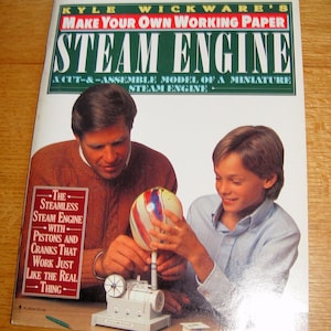 May include: A book cover with the title "STEAM ENGINE" and the text "MAKE YOUR OWN WORKING PAPER". The cover shows a man and a boy assembling a model steam engine. The model is white and gray.