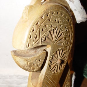 May include: A wooden nutcracker carved with intricate geometric patterns. The nutcracker is made of light brown wood and has a rounded head with a small opening for cracking nuts.