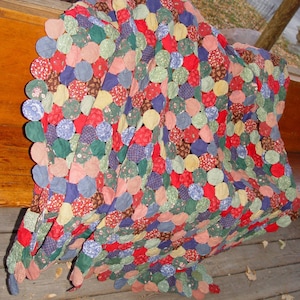 May include: A colorful handmade quilt with a unique design. The quilt features a pattern of overlapping circles in various colors and patterns, including red, green, blue, and floral prints. The quilt is draped over a wooden surface.