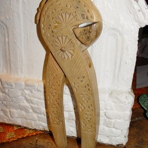 May include: A wooden nutcracker with intricate carvings. The nutcracker is brown and has a detailed design on the handles and the nut-cracking part.