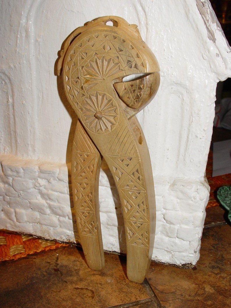 May include: A wooden nutcracker with intricate carvings. The nutcracker is brown and has a detailed design on the handles and the nut-cracking part.