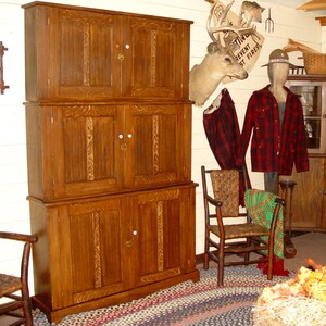 May include: A large, three-section wooden cabinet with four doors in a rustic setting. The cabinet is a warm brown color and has white knobs. A woven chair, plaid blanket, and a deer head mount are also visible.