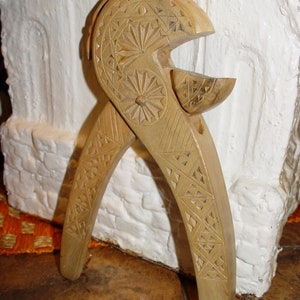 May include: A wooden nutcracker with intricate carvings. The nutcracker is shaped like a pair of pliers with a carved design on the handles and a small bowl at the top.