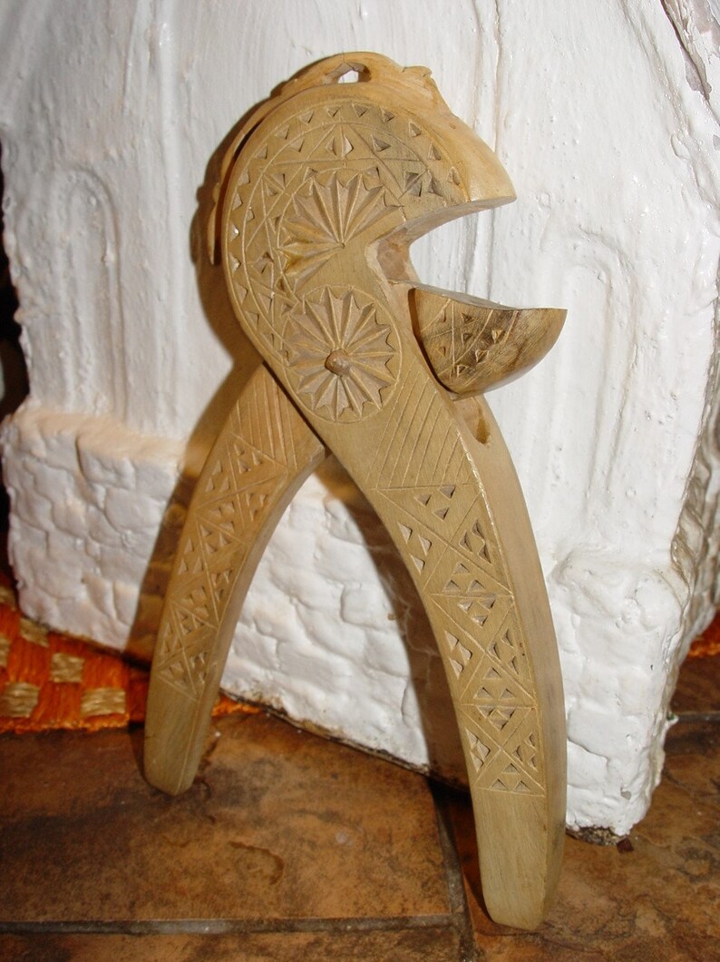 May include: A wooden nutcracker with intricate carvings. The nutcracker is shaped like a pair of pliers with a carved design on the handles and a small bowl at the top.
