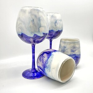 May include: Three wine glasses with a white and blue marbled design. The glasses are clear and have a purple stem and base.
