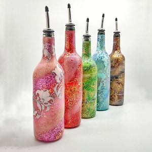 May include: Five glass bottles with decorative designs and silver pour spouts. The bottles are pink, red, green, blue, and brown. Each bottle has a different floral design.